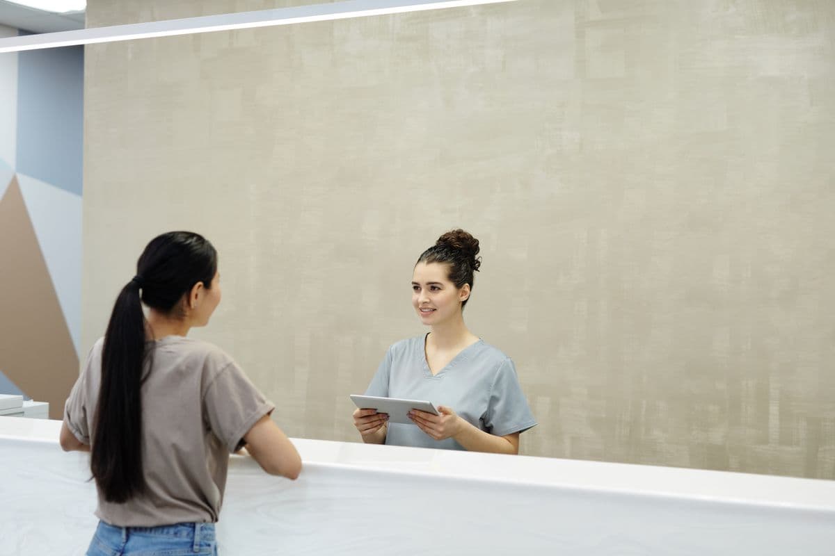 A clinic receptionist with a tablet welcoming a patient