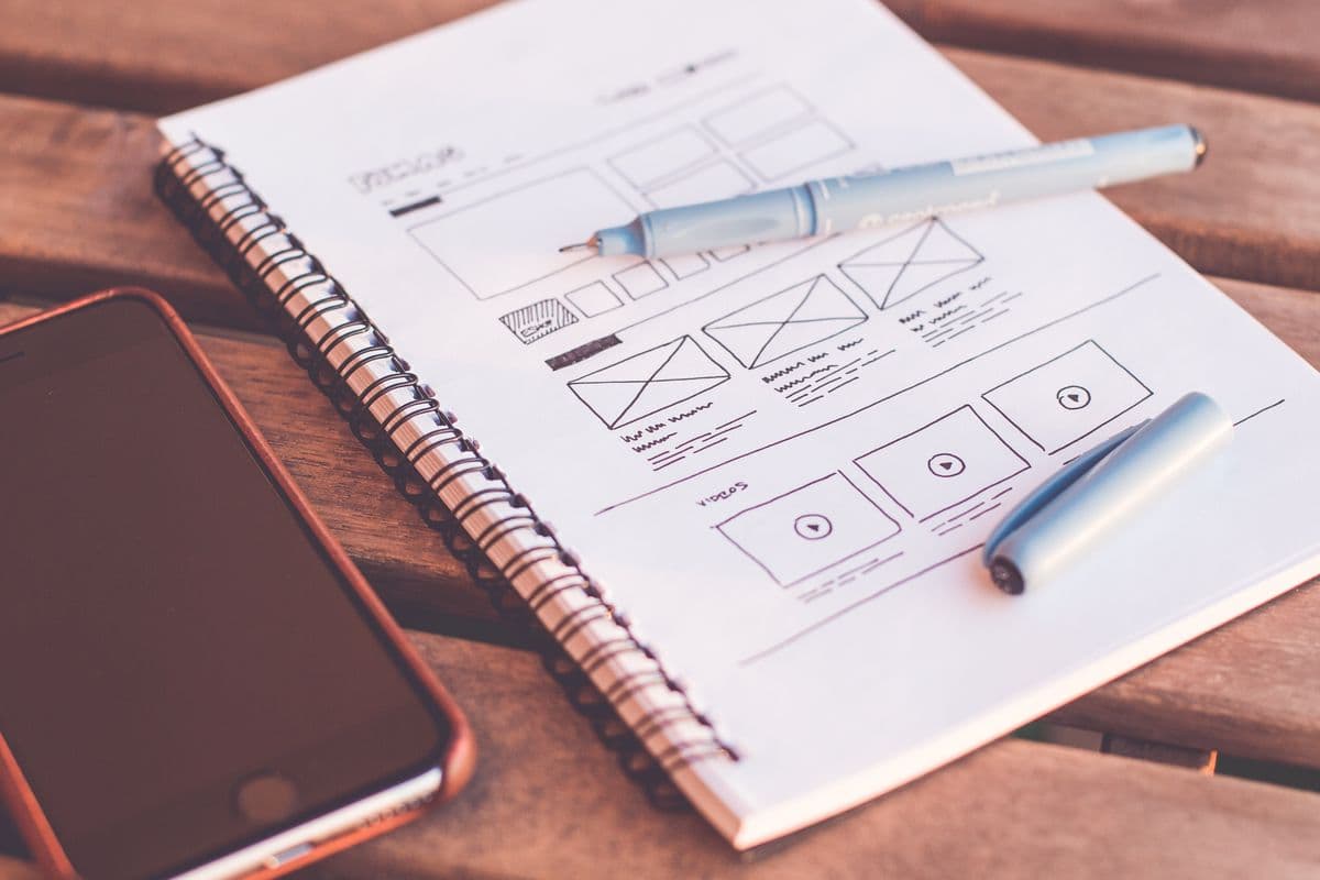 Website wireframes sketched in a notebook next to a phone